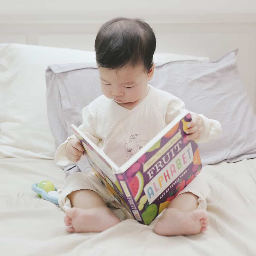Photo of young child reading a picture book in bed.