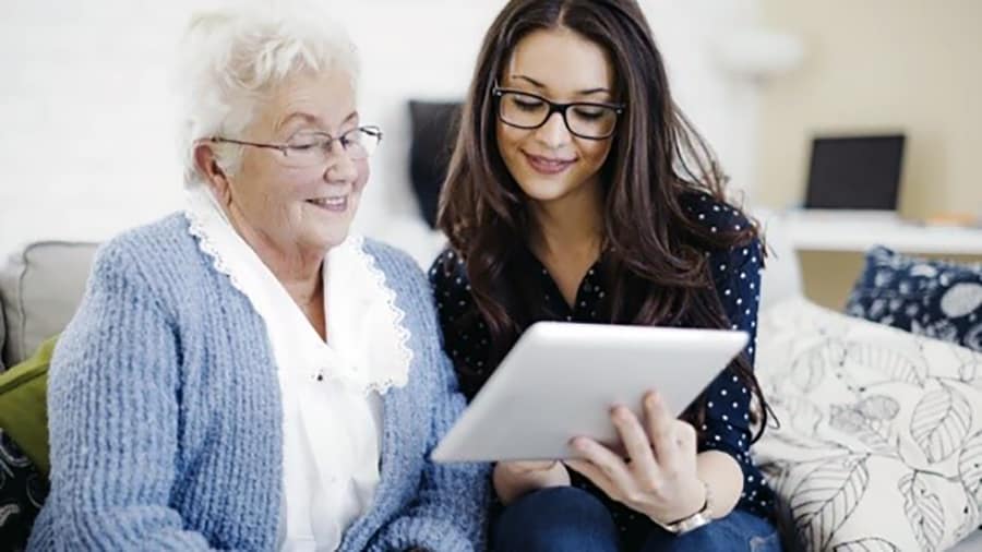 Photo of older woman being shown by younger woman how to use a tablet.