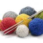 photo of knitting needles with eight balls of coloured wool