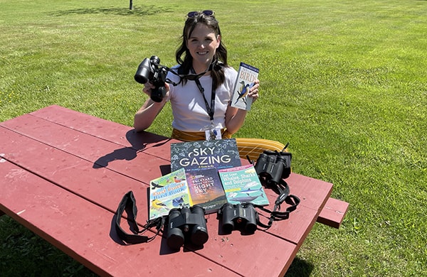 Lydia Hunsberger of Western Counties Regional Library sits at a picnic table with the library binocular kits spread out on the table.