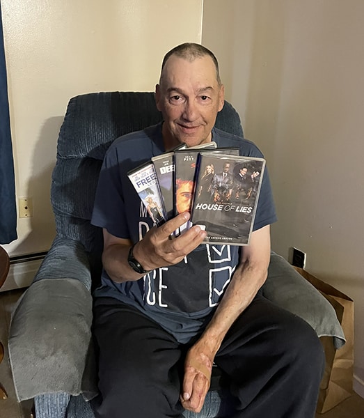photo of man smiling and sitting in a chair holding four DVDs