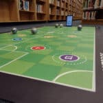 floor mat with soccer pitch on it and round ball-shaped robots in the library