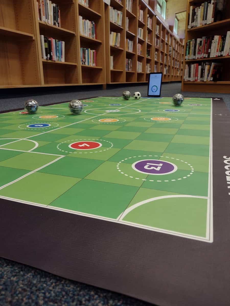 floor mat with soccer pitch on it and round ball-shaped robots in the library
