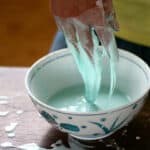 hands dripping with light blue goo above a bowl