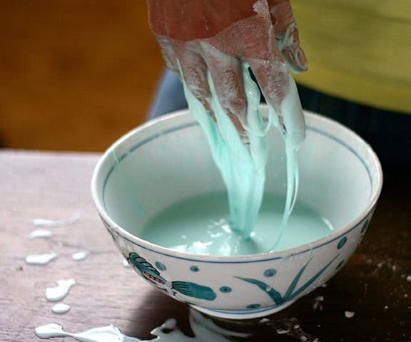 hands dripping with light blue goo above a bowl