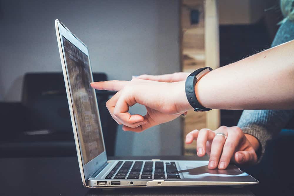 one hand pointing to the screen of a laptop and another hand pressing the navigation pad.