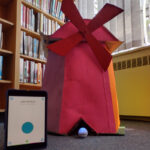 a small spherical robot in front of a red windmill and a stack of books.