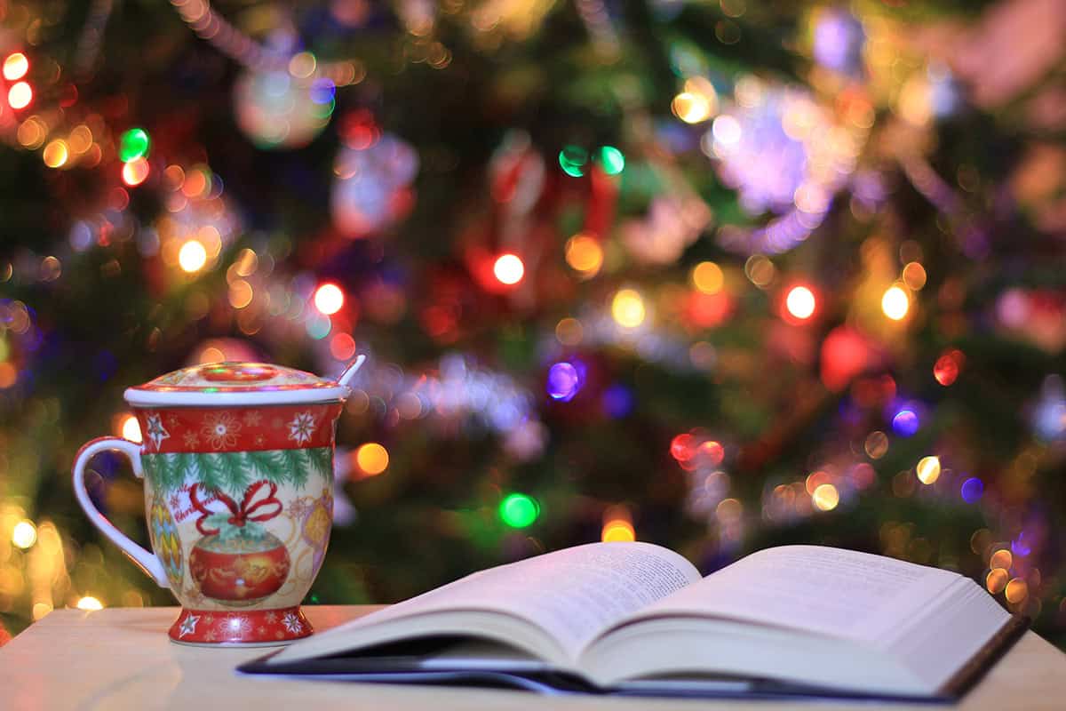 open book next to a Christmas mug with a tree in the background