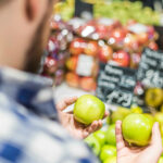 image of man holding two green apples in a store