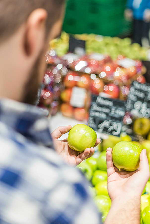 image of man holding two green apples in a store