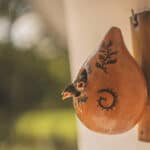 Two small birds sticking their heads out of a gourd birdhouse.