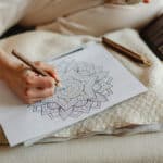 A hand holding a pencil colouring in a mandala.