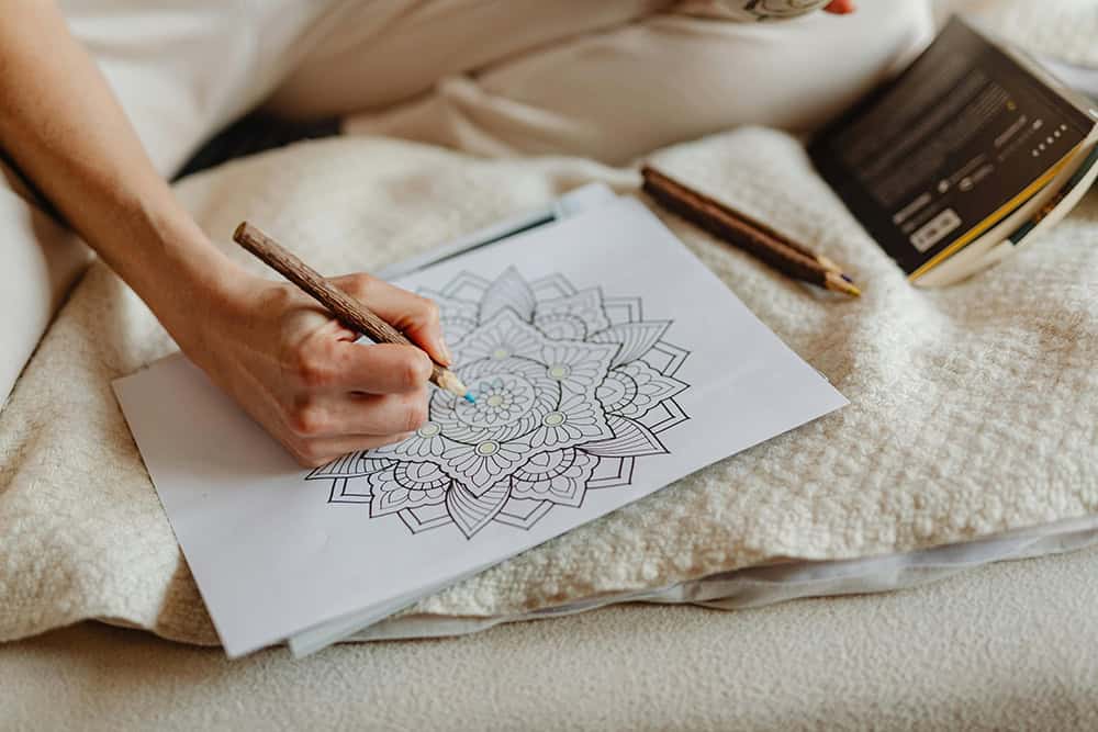 A hand holding a pencil colouring in a mandala.