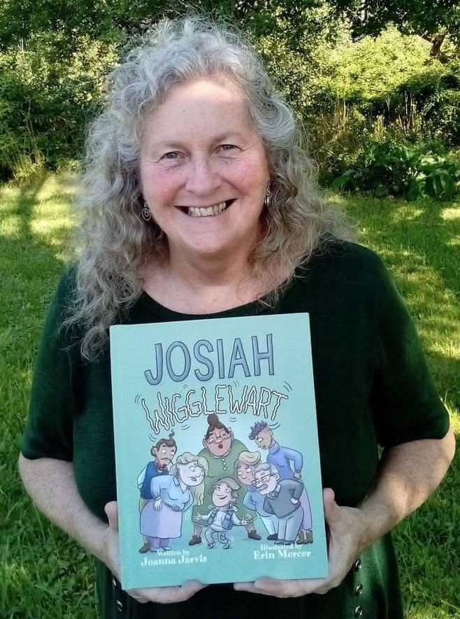 image of a woman with long, grey hair wearing a black top and holding a children's book with the text 'Josiah Wigglewart'