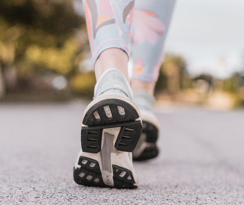 photo of legs and running shoes of a person walking on a road.