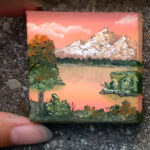 image of fingers holding a tiny painting on canvas