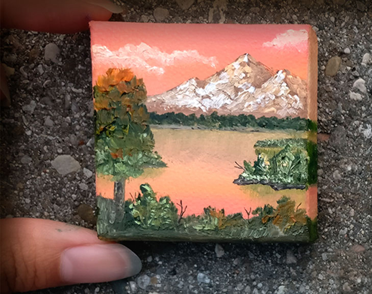 image of fingers holding a tiny painting on canvas