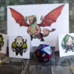 image of three cardboard pieces with creatures on them and a two multi-sided die