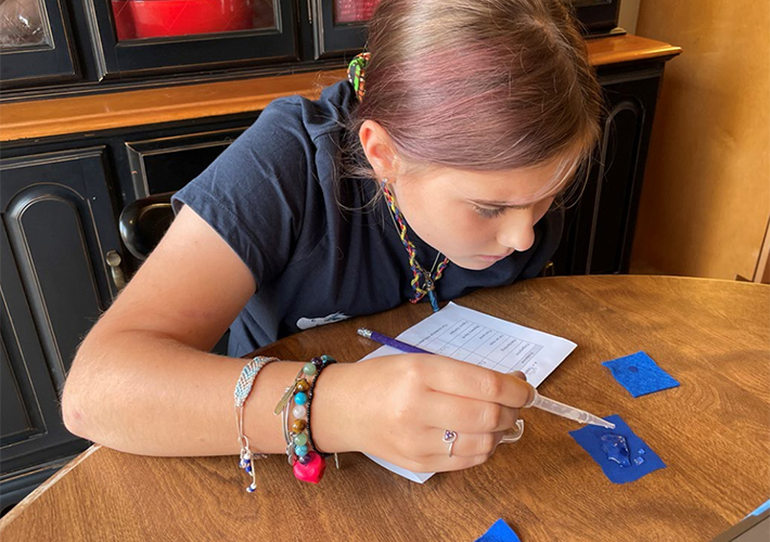 image of a girl using an eyedropper to drop liquid onto a blue slide.