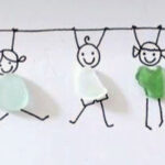 five pieces of sea glass on a paper with drawings of five stick figures holding a line