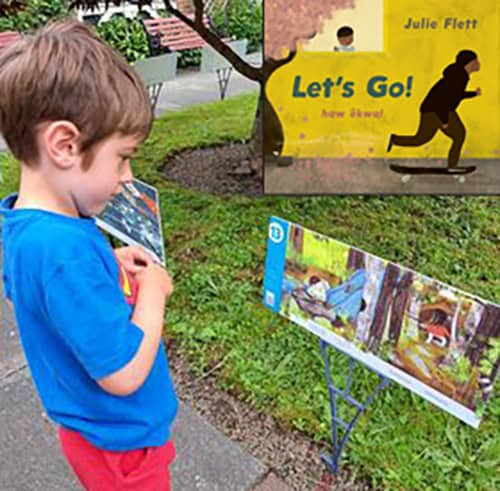 image of a boy standing in a courtyard reading a large story board with the image of a book cover in the top right corner.