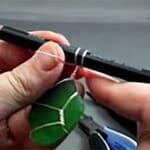 image of two hands holding a pencil with wire wrapped around it and a piece of green sea glass