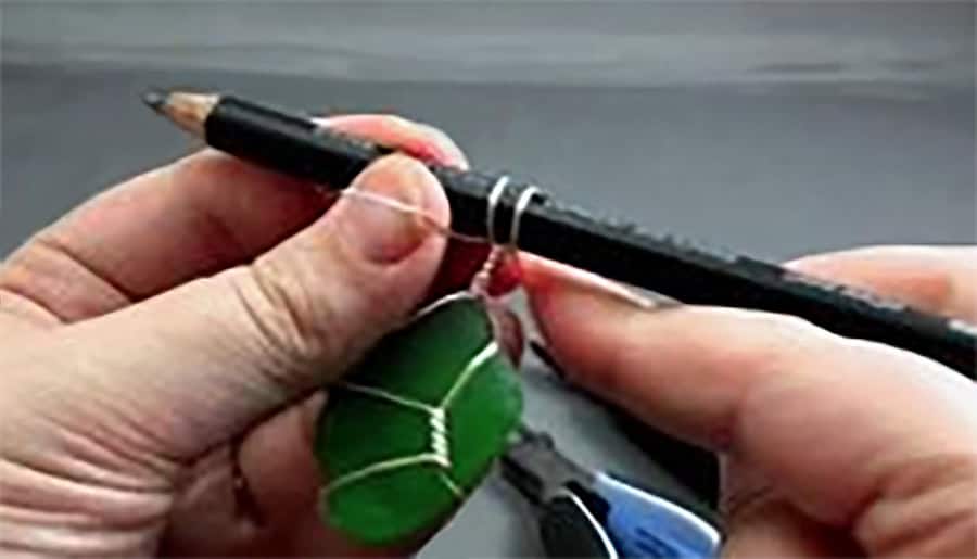 image of two hands holding a pencil with wire wrapped around it and a piece of green sea glass