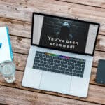 image of a laptop computer on a desk with the text 'You've been scammed'