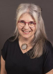 image of a woman with long blonde hair and glasses wearing a black top.