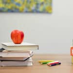 image of an apple on a stack of books on a desk and three letter blocks.