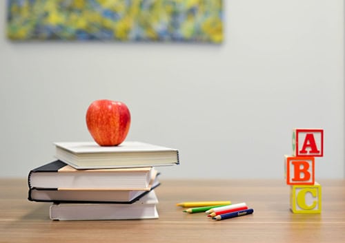image of an apple on a stack of books on a desk and three letter blocks.