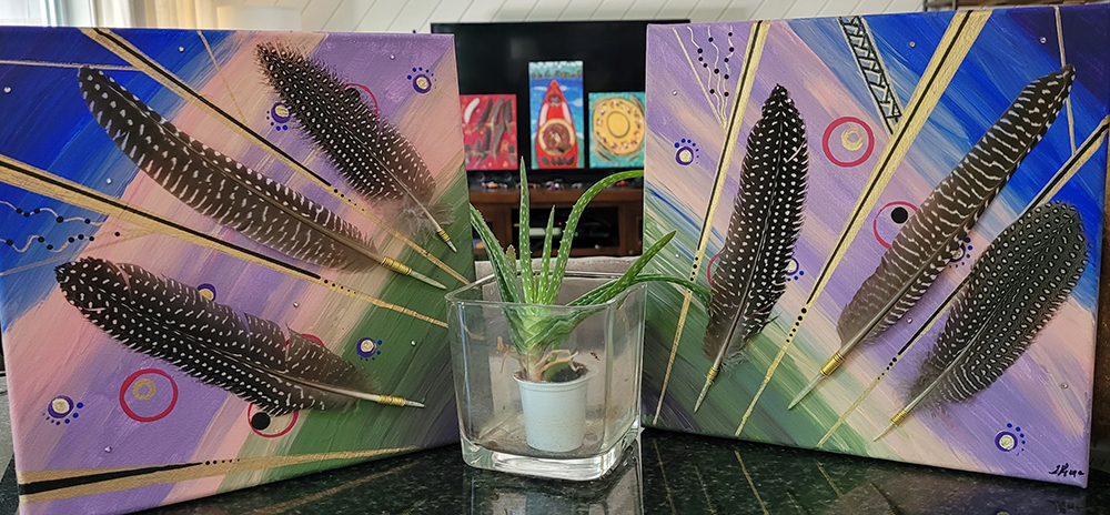 image of an aloe plant in a clear pot between two pieces of art featuring feathers.