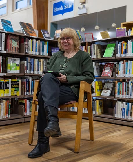 image of older woman wearing glasses sitting in a chair holding a book