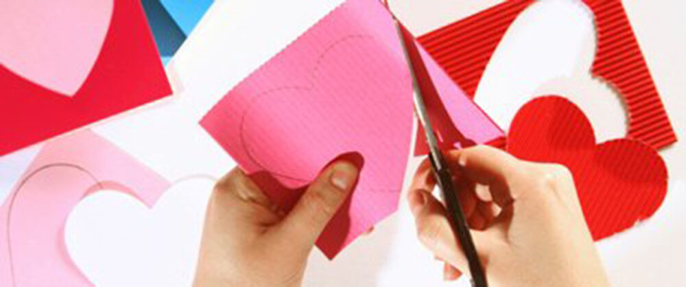 image of a pair of hands cutting pink construction paper into hearts.