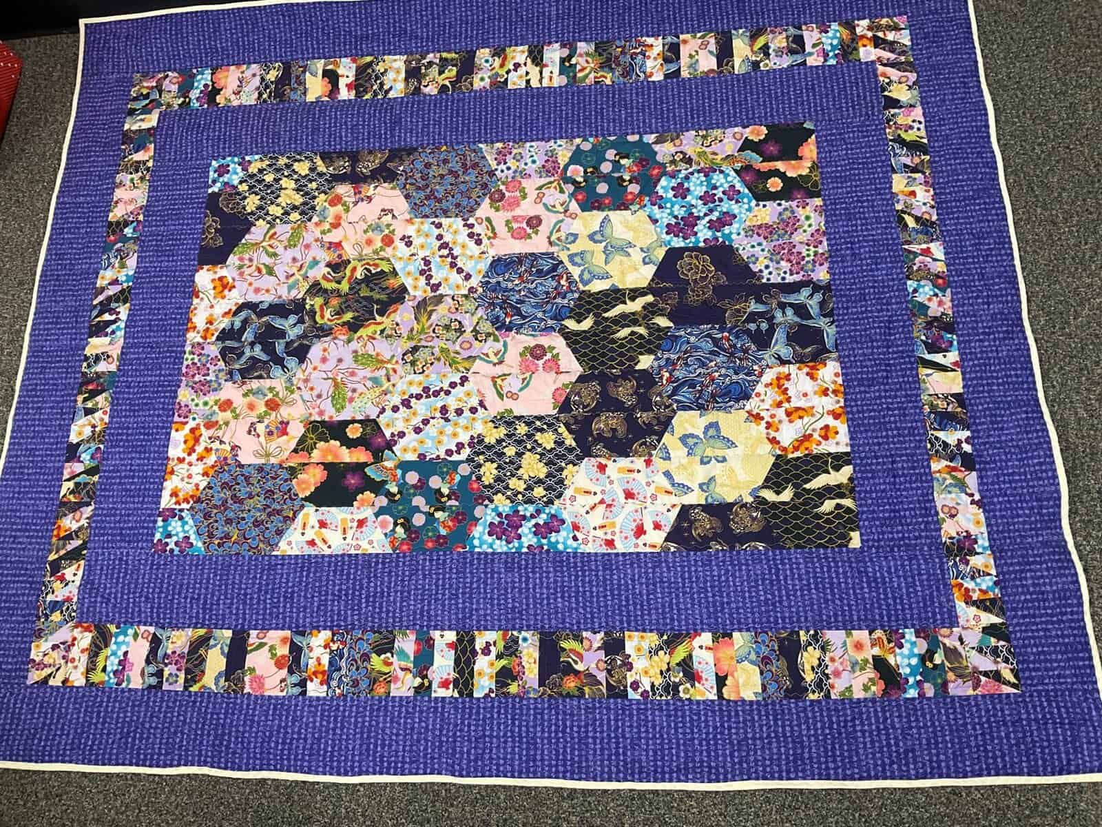 A blue quilt featuring hexagon shaped patches. The patches have floral and traditional Japanese cloth patterns.