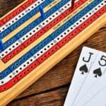A cribbage board on a wooden table. Next to it are the jack of spades, five of spades, and five of diamonds cards.