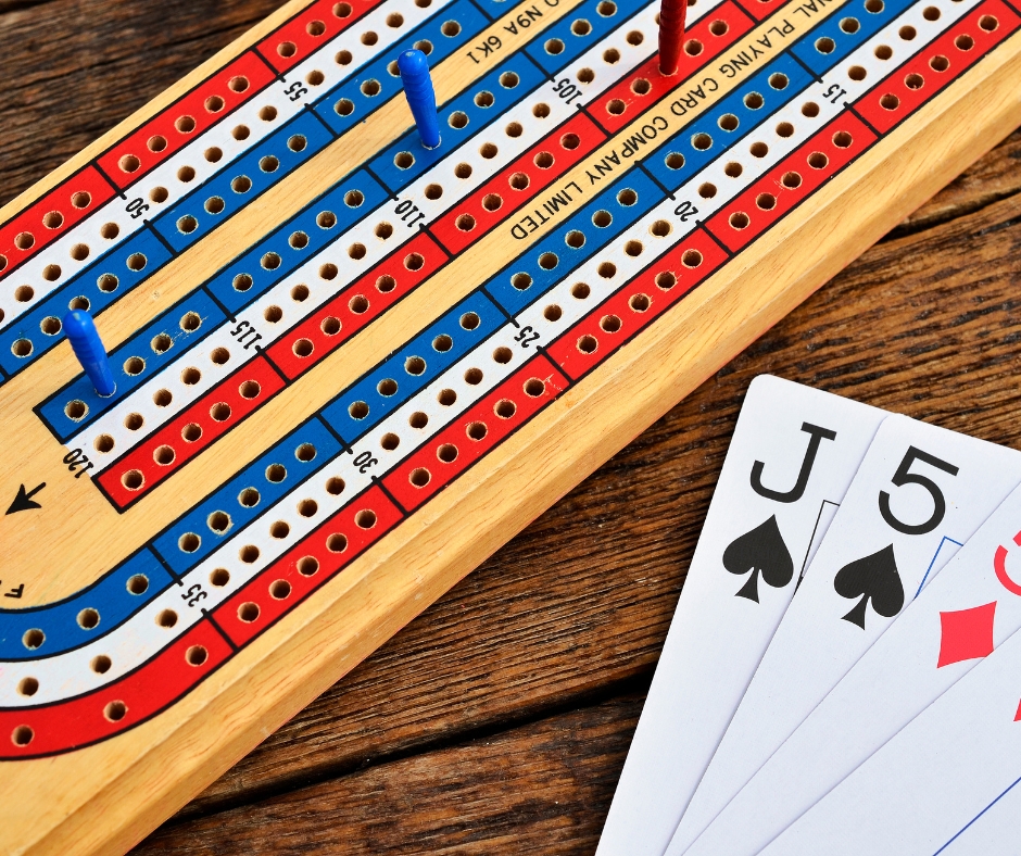 A cribbage board on a wooden table. Next to it are the jack of spades, five of spades, and five of diamonds cards.
