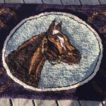 A rug hooking of a brown horse head. The outline is deep purple with horseshoes pointing towards the horse in the centre.