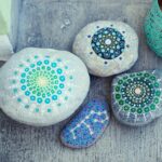 Four mandala stones painted in tones of blue. Three have circular patterns and one looks like a constellation.