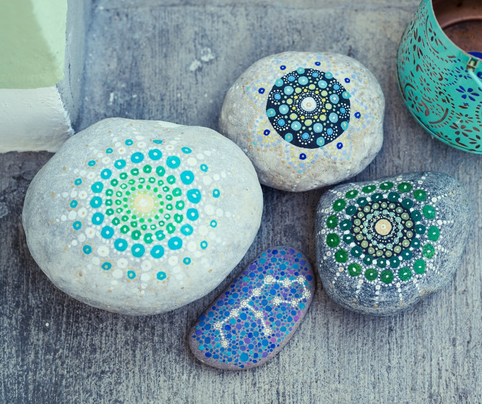 Four mandala stones painted in tones of blue. Three have circular patterns and one looks like a constellation.