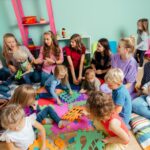 A group of moms and their young children sitting on foam mats and talking.