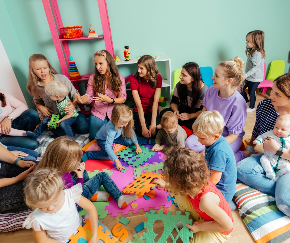 A group of moms and their young children sitting on foam mats and talking.
