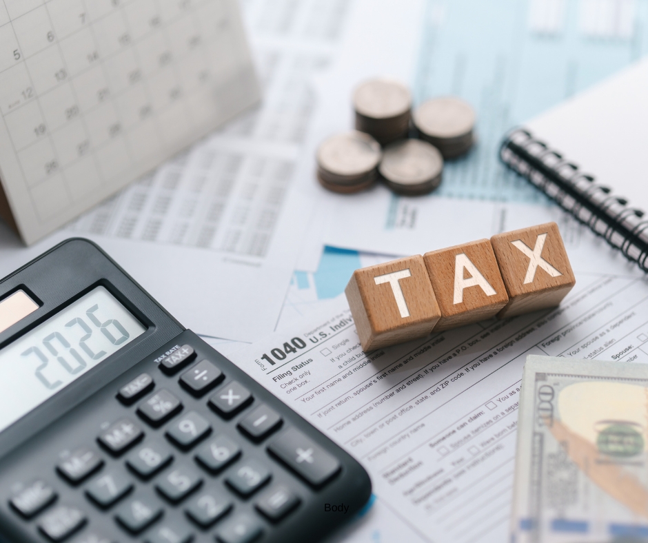 Financial papers scattered on a table. There is also a calendar, coins, a notebook, and "TAX" spelled out with wooden blocks.