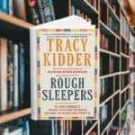 The cover is light yellow with a dashed boarder. The dashes are in red, blue, and a darker yellow. Behind the cover are shelves of books.