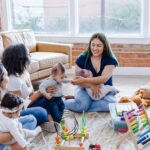 Three young women and their babies playing with block toys on the floor. They are smiling and talking to each other.