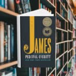 The cover says James but the J is very long and at the bottom of the letter is a sketch of a man with a bindle stick. You cannot see his head. Behind the cover are shelves of books.