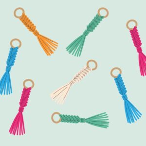 Seven cartoon macramé keychains in various colours. There are pink, green, blue, orange, and white ones scattered about.