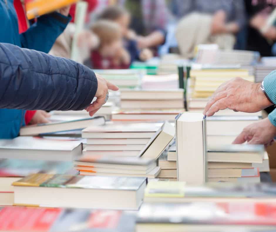 A table absolutely filled with books. People surround the table and pick through the available books.