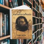 The cover has a drawn image of a giant bug with a disturbing man's face. Behind the cover are shelves of books.