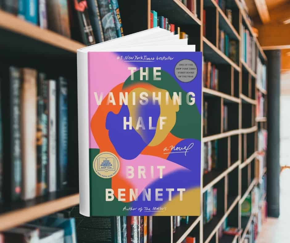 The cover features an abstract interpretation of two women leaning into each other. Their faces, bodies, and hair, are made of different coloured shapes. Behind the cover are shelves of books.